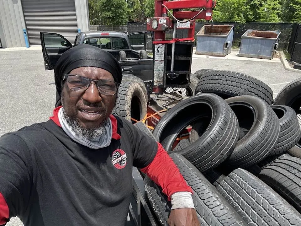 Bobby Cato in a Cato's Tire shirt, standing beside a trailer stacked with tires outside the shop.